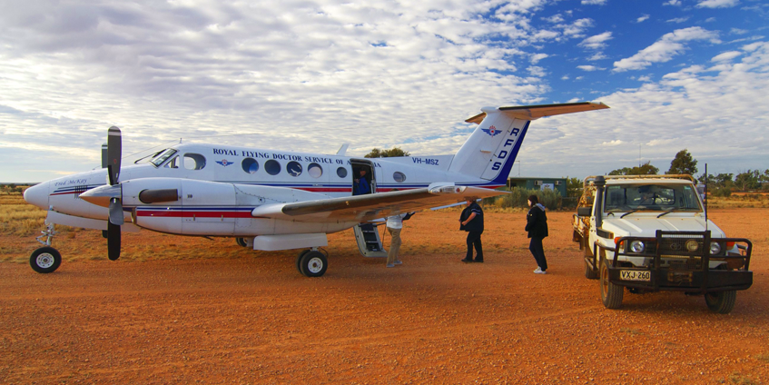 RFDS aircraft on red dirt runway with 4wd and two people aproaching plane