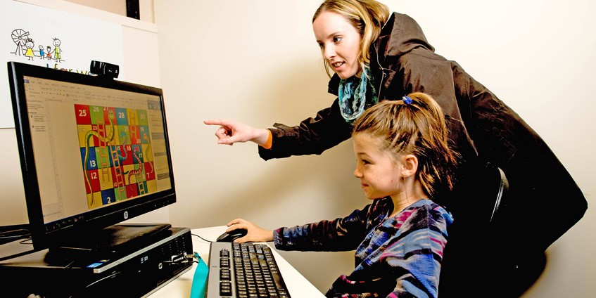 Young woman helping a young girl use a computer