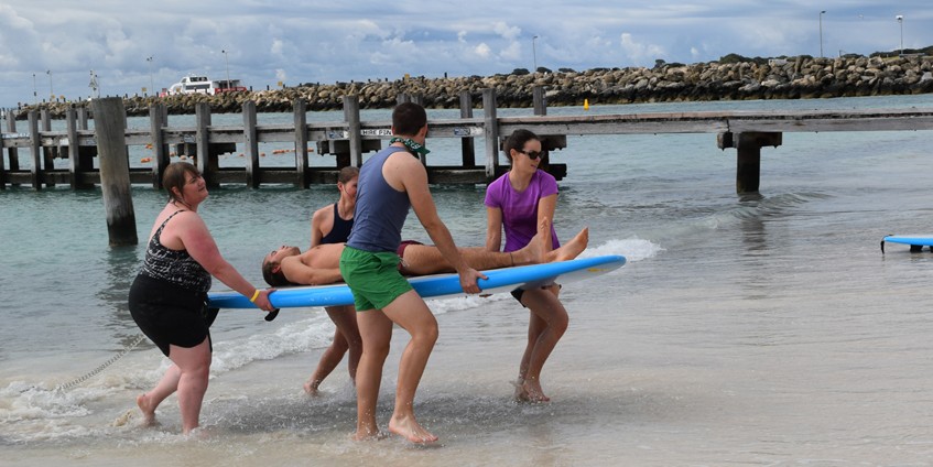 People carrying a person on a surfboard out of the ocean.