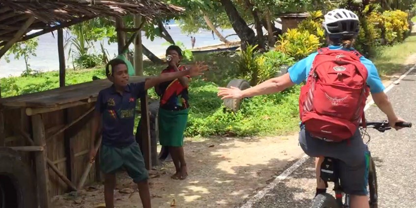Person riding a bike and high fiving local PNG boy