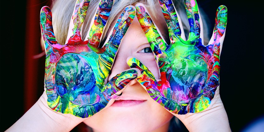 Boy with coloured paint on hands in front of his face