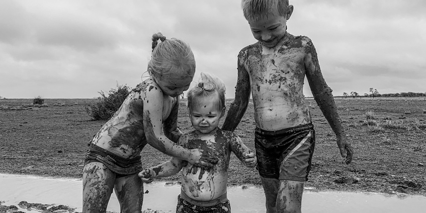 Three children playing in the mud in the first decent rainfall they have seen since March 2018