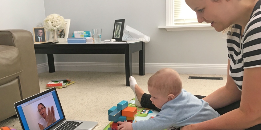 Baby playing with blocks in front of laptop supported by mother