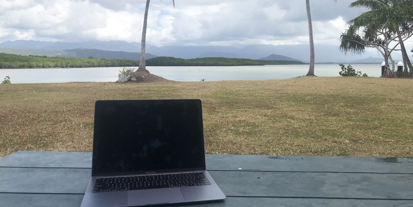 Laptop besides tropical coastline with palm trees