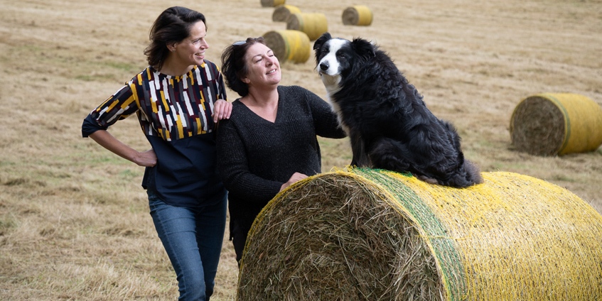 Two women with dog on a hay bail.