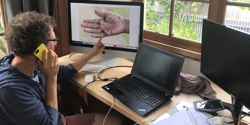 Man on phone diagnosing a hand on computer screen. Dr John Kelly conducting a telehealth consultation.