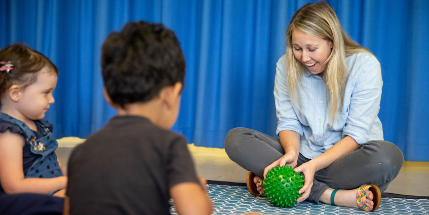 Woman playing with two younger children with a ball