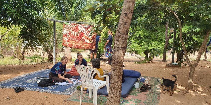 Community Allied Health Team seated under trees talking to locals