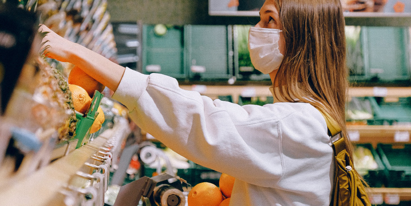 Young woman reaching for fruit on a shelf wearing a mask