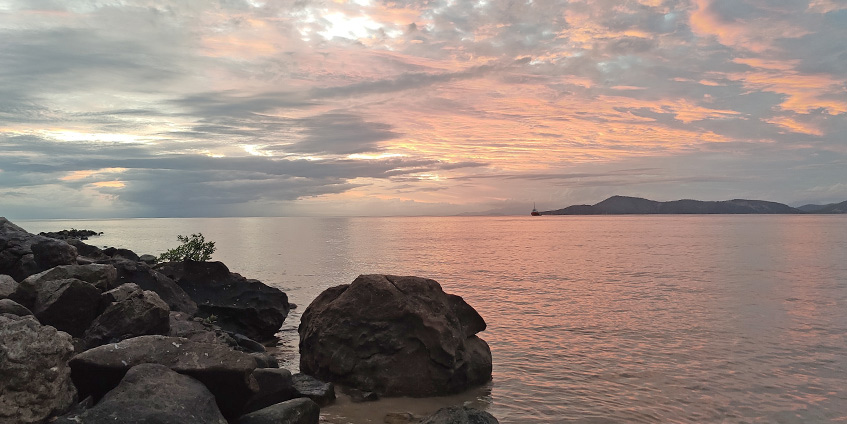 Palm Island, Queensland. Orange sunset by the coast with rocks in the foreground.