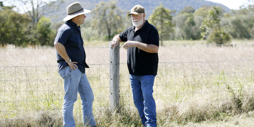 Two men standing by a fence post on a grassy property