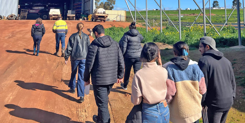 Students walking towards farm shed with industrial sprinkler in the background