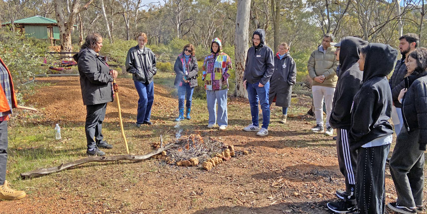 Welcome to country ceremony being performed in front of multiple students in a bush setting