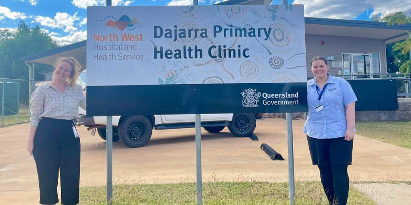 Two medical women standing either side of a Dajarra Primary Health Clinic sign