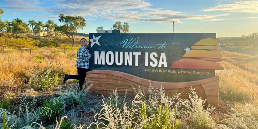 Medical student standing next to Mt Isa township road marker sign