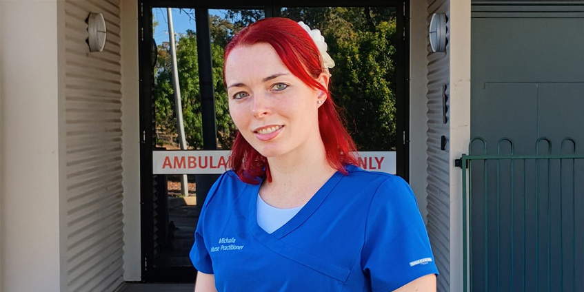 Michaila MacAskill in blue medical clothes in front of medical building