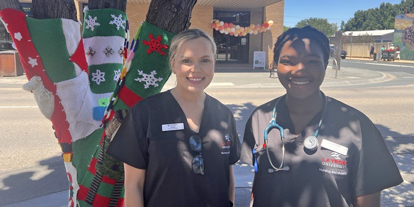 Two nurses in dark medical garments posing outside a rural town street.
