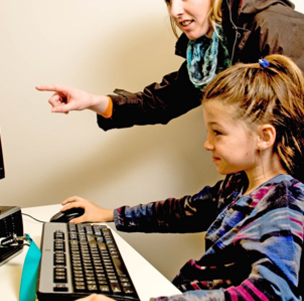 Young woman helping a young girl use a computer