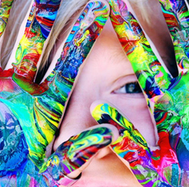 Boy with coloured paint on hands in front of his face
