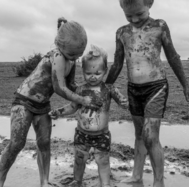 Three children playing in the mud in the first decent rainfall they have seen since March 2018