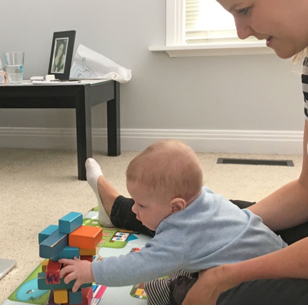 Baby playing with blocks in front of laptop supported by mother