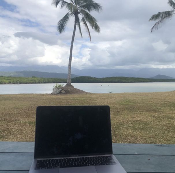 Laptop besides tropical coastline with palm trees
