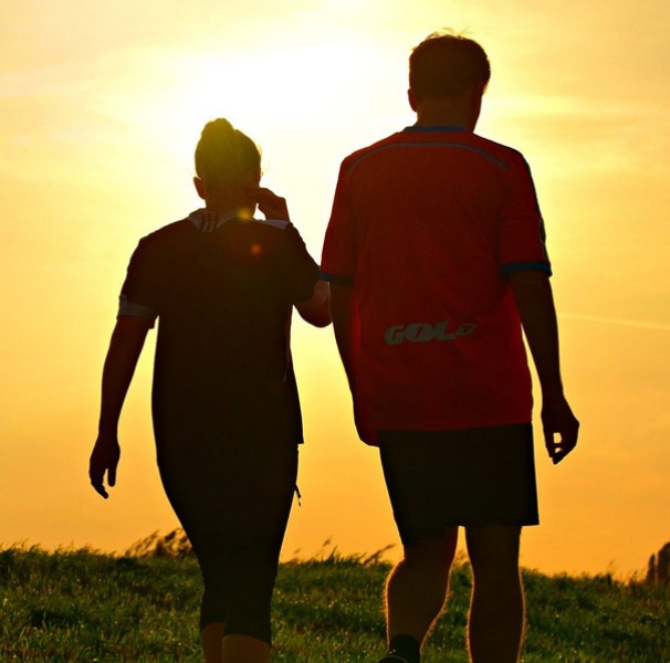 Silhouette of man and woman excercising against a orange sky