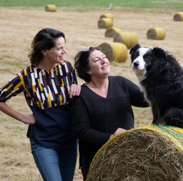 Two women with dog on a hay bail.