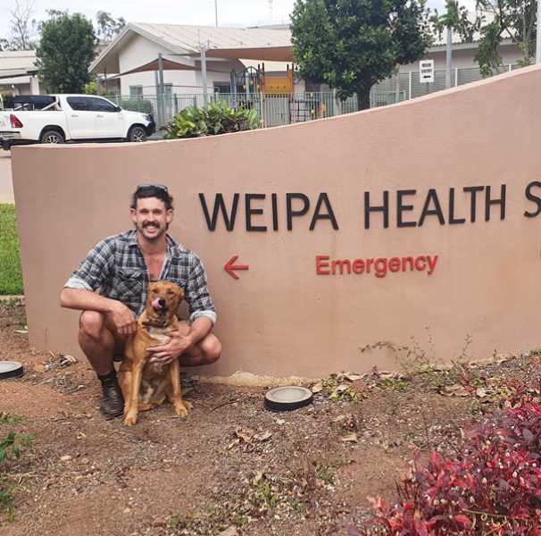 Man and his dog in front of Weipa Health Services sign
