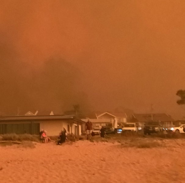 Bushfire smoke filled sky shadowing evacuees on the beach