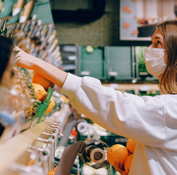 Young woman reaching for fruit on a shelf wearing a mask