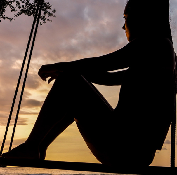 Silhouetted woman sitting on swing at sunset