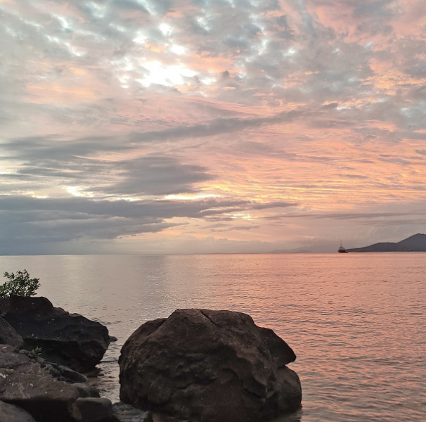 Palm Island, Queensland. Orange sunset by the coast with rocks in the foreground.