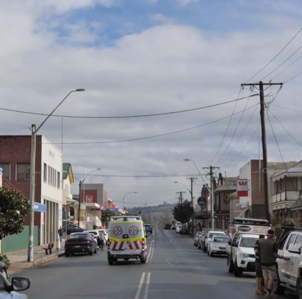 Rural street with cars parked each side an ambulance drives doen the middle
