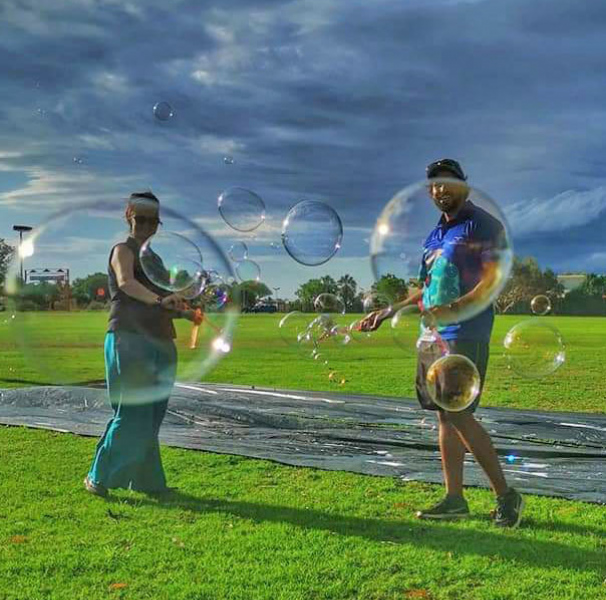 Two people blowing bubbles in a football field