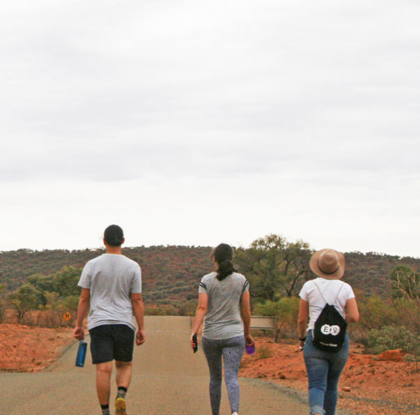 Three people walking down remote red earth road.