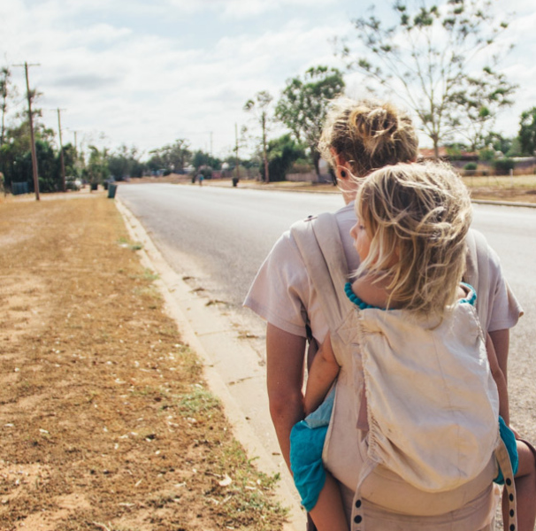 Woman carrying daughter hiking down rural street