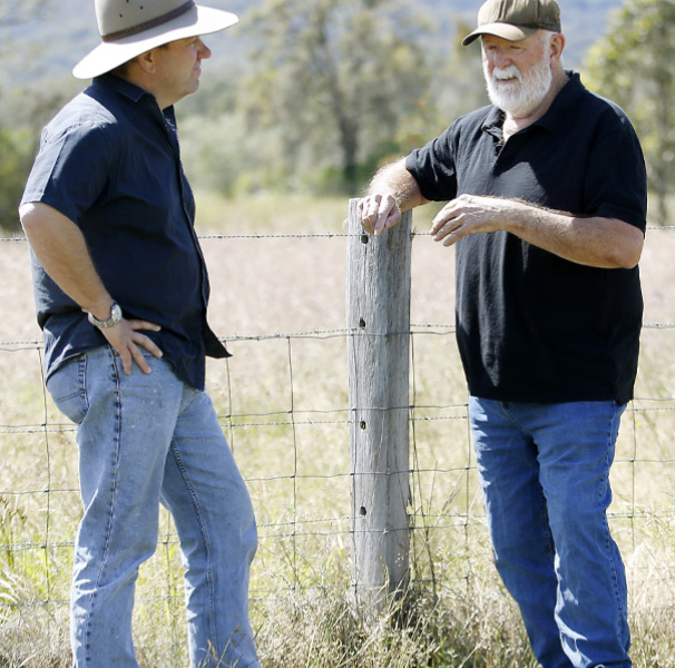 Two men standing by a fence post on a grassy property