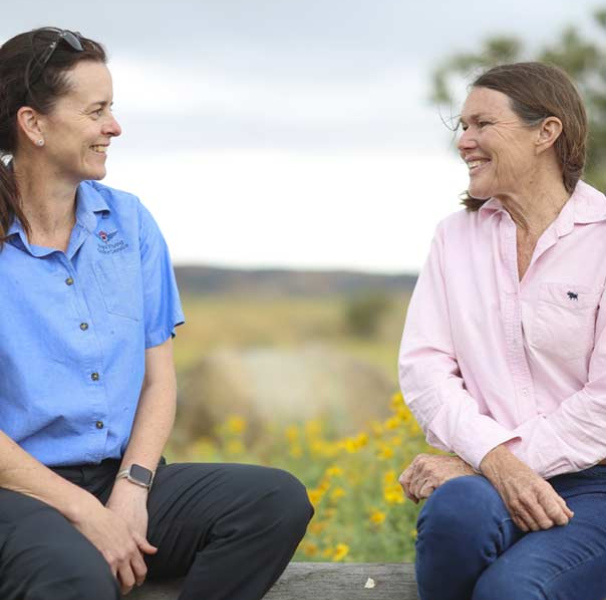Two women talking outside in a grassy field.