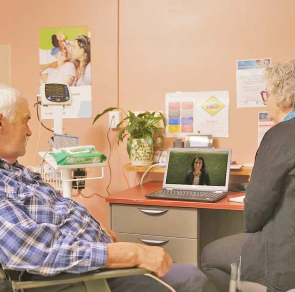 Older man in chair looking at laptop with woman at desk
