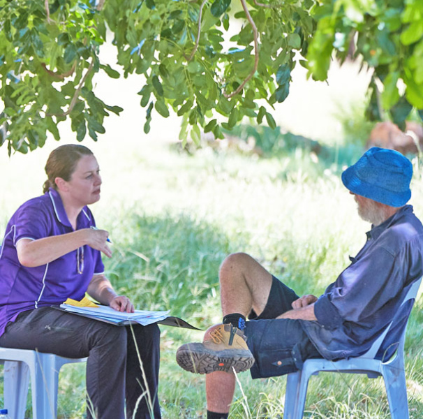 Woman talking to man whilst seated out doors with tree branch overhead.