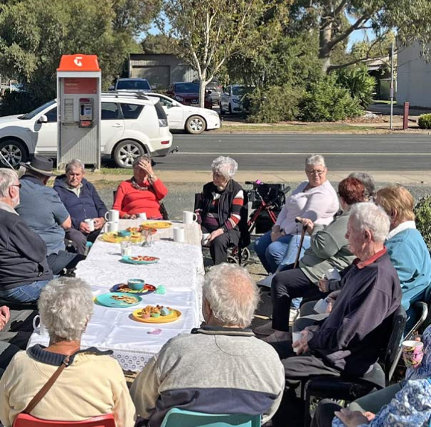 Group of people seated outside at a large table having tea