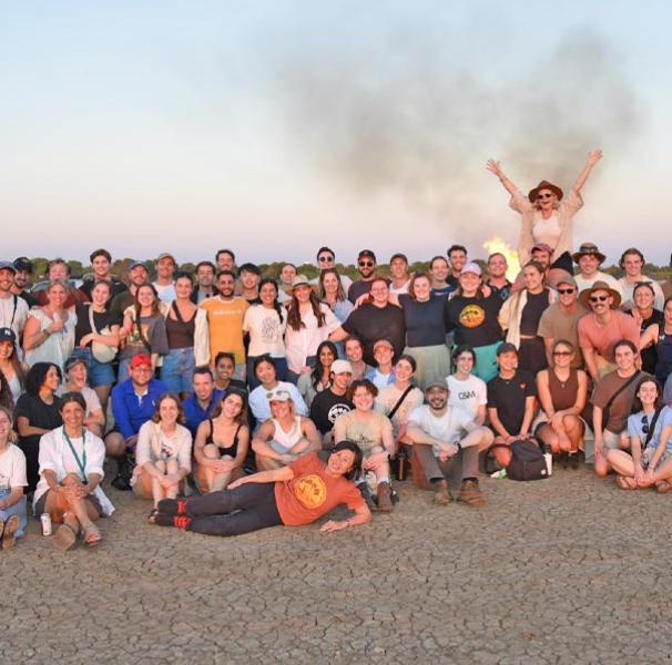 Large group of people on a beach with a fire behind
